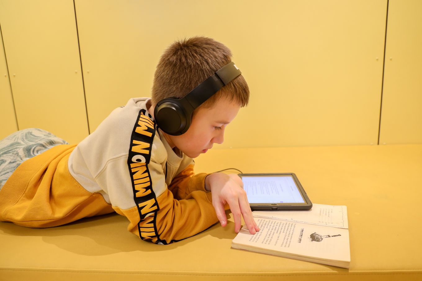 En elev med hodetelefoner som lytter til tekst på læringsbrettet og leser i en bok