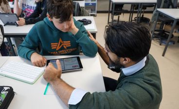 En lærer veileder en elev som arbeider på læringsbrettet.