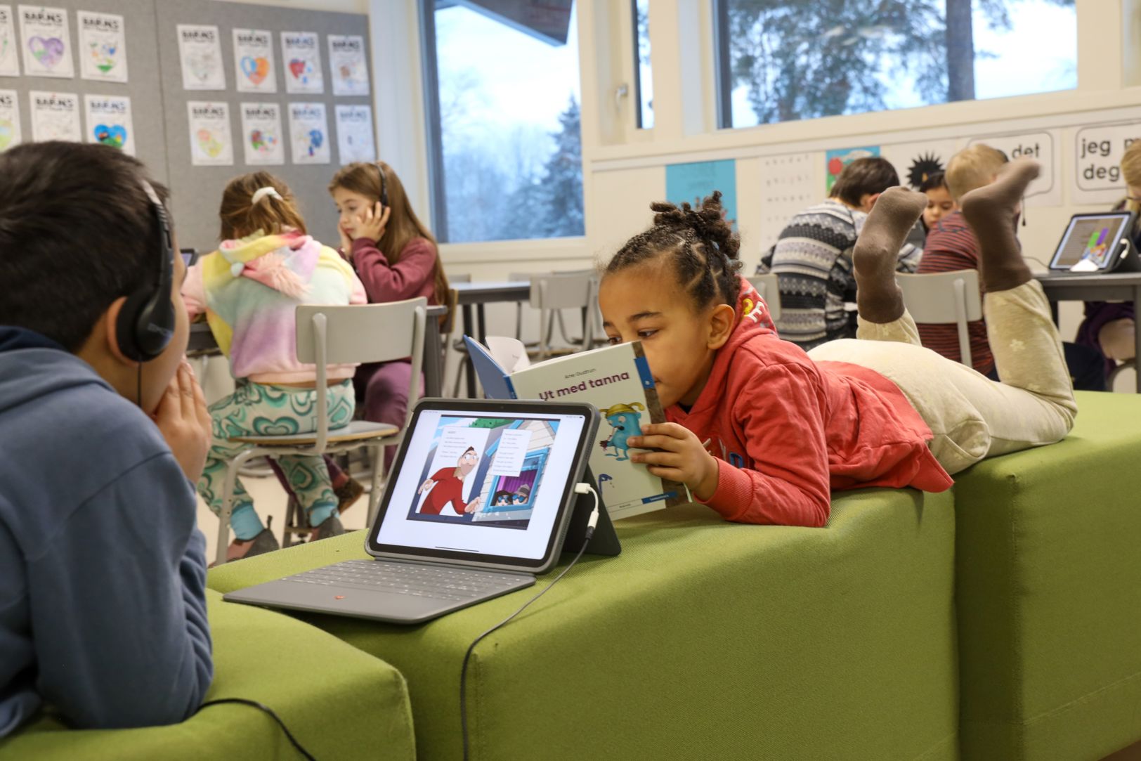 Elever som leser i et klasserom. Noen leser i bok og noen på læringsbrett. 
