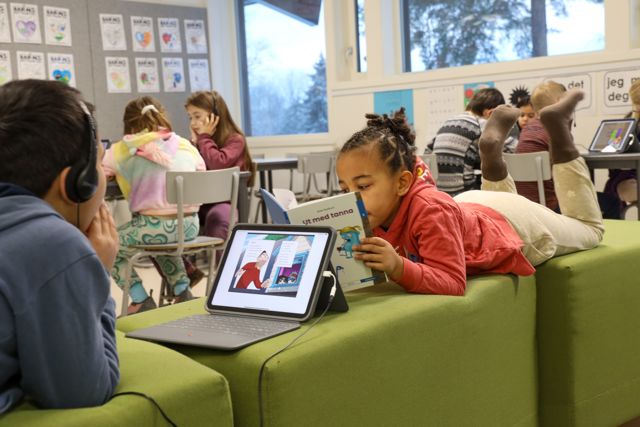 Elever som leser i et klasserom. Noen leser i bok og noen på læringsbrett. 