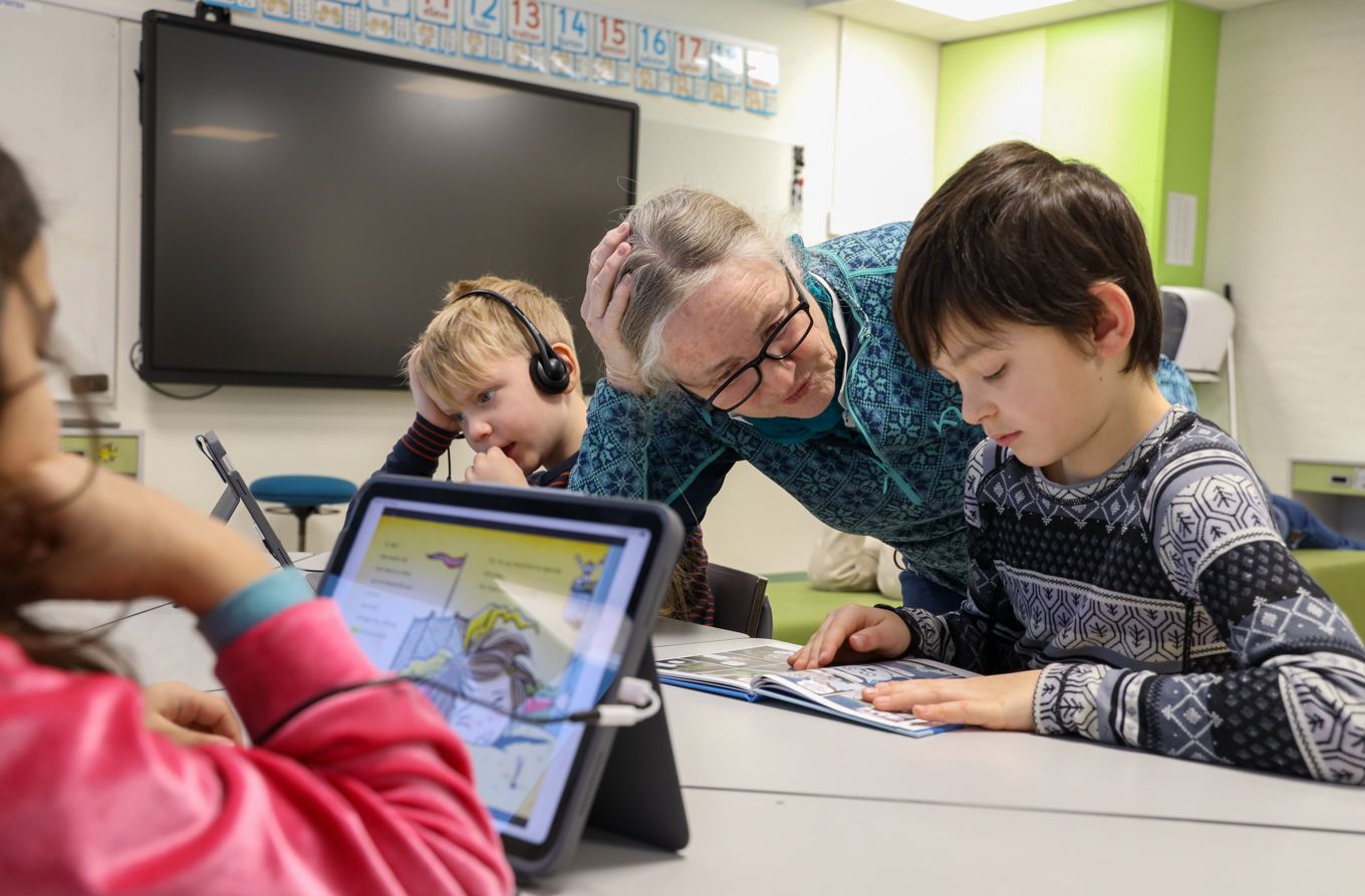 En lærer og noen barn som leser, i bok og på læringsbrett.