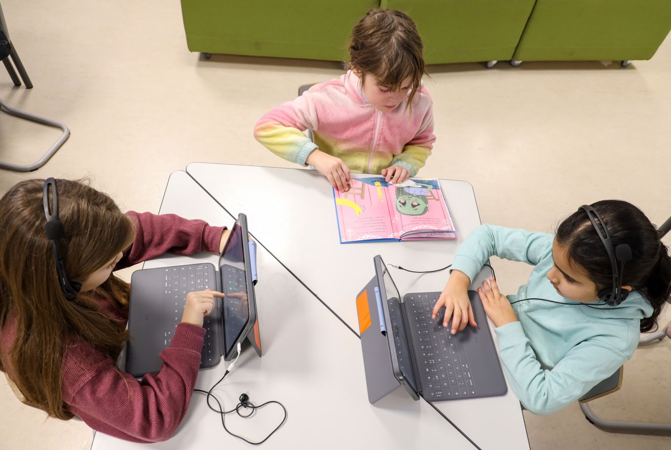 En gruppe barn som sitter ved et bord og leser, i bok og på læringsbrett