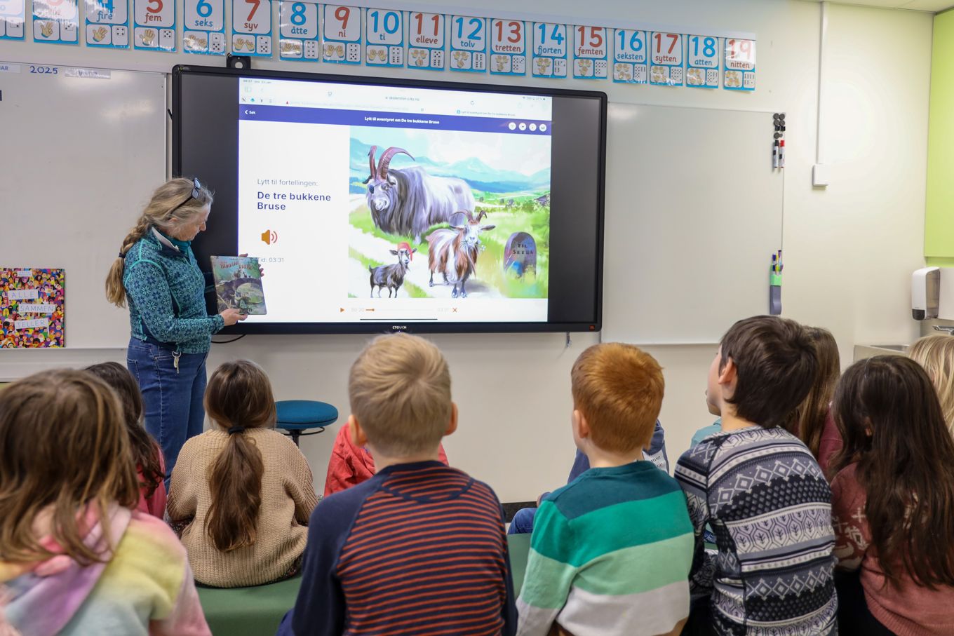 En lærer som leser for klassen og viser bilder fra boka på digital tavle