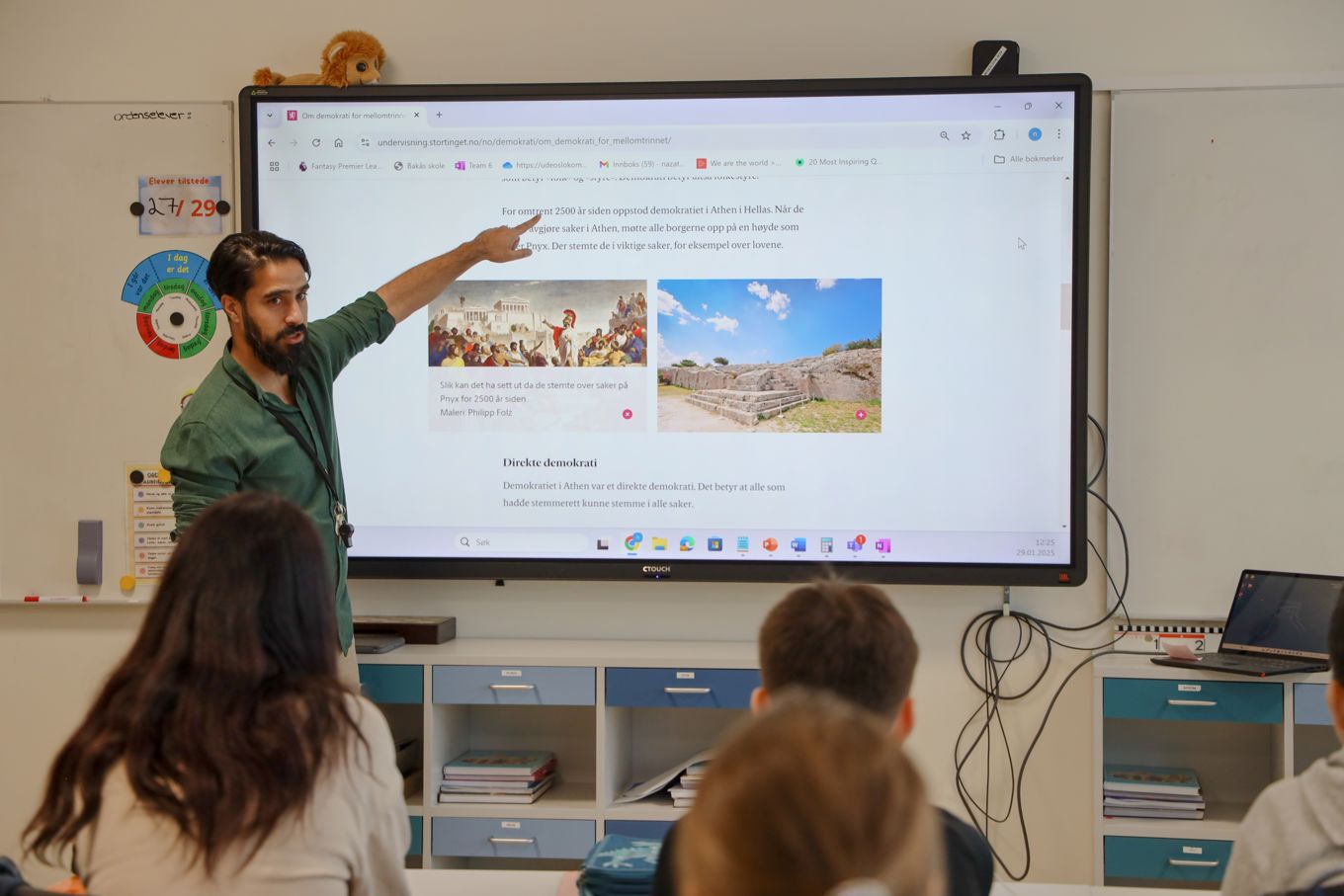 En lærer som underviser i klasserommet, læreren peker i teksten på digital tavle