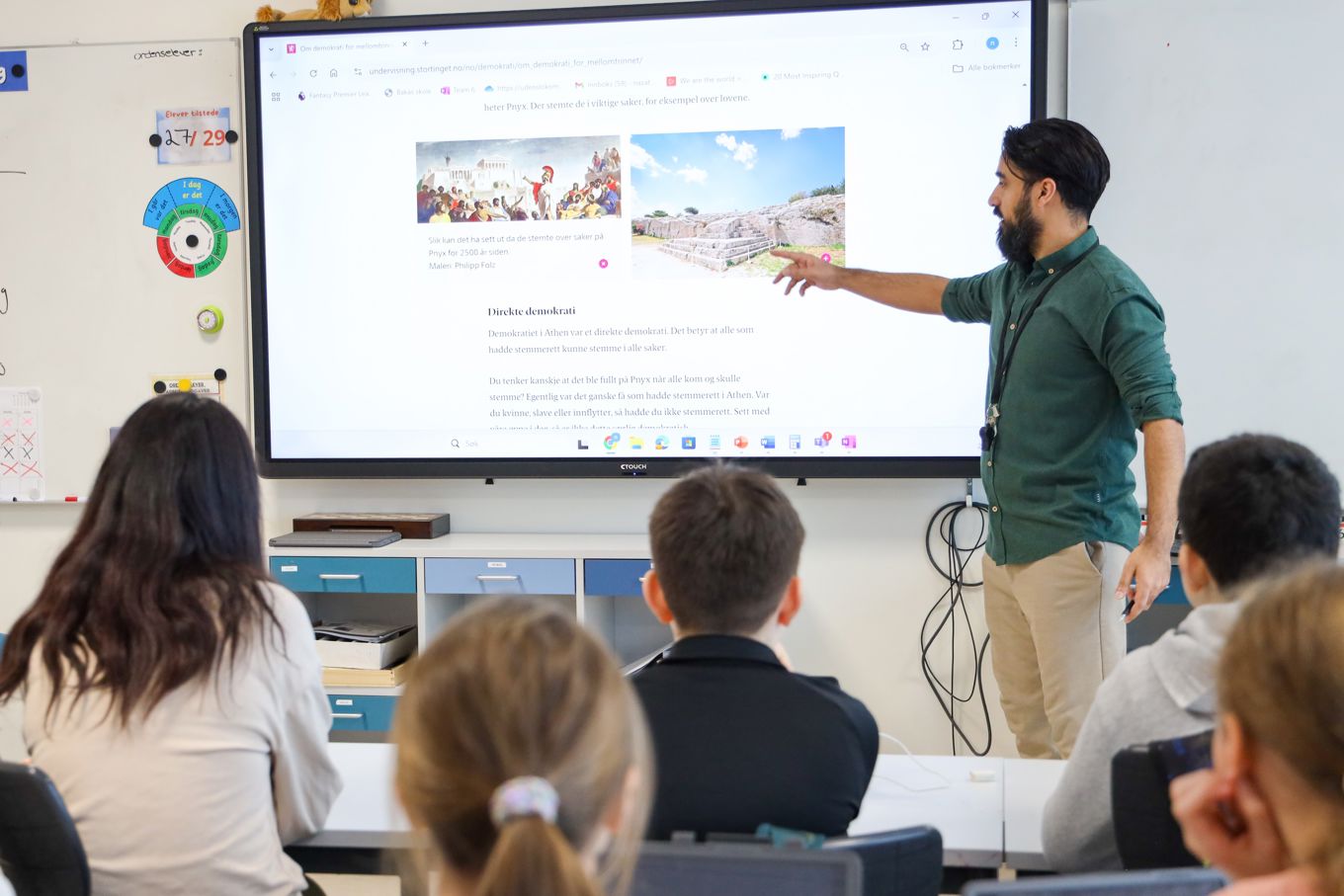 En lærer som underviser en klasse og peker på digital tavle