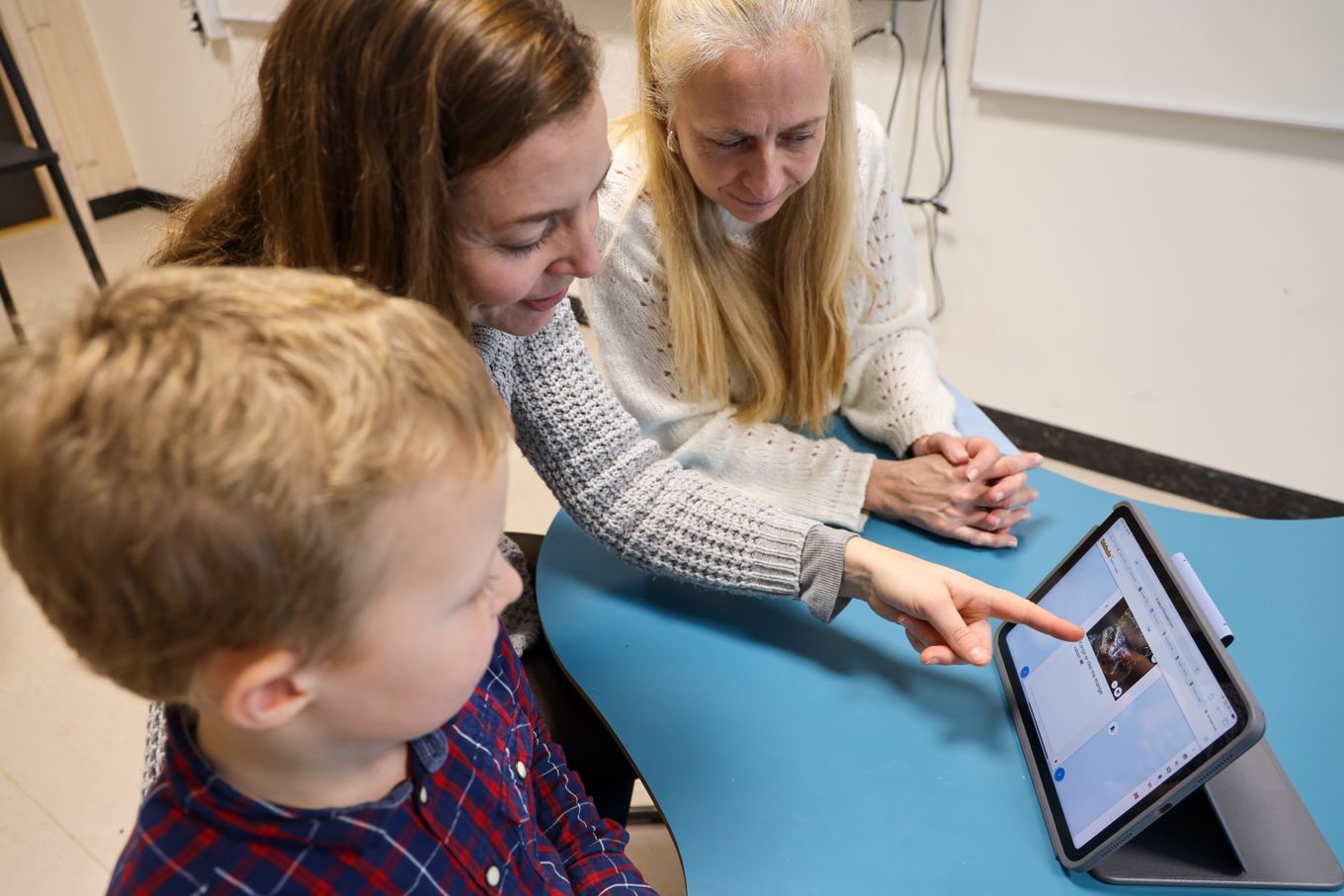 En elev, en mor og en lærer på utviklingssamtale, de ser på et læringsbrett og moren peker på elevens arbeid