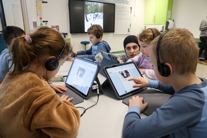 Elever som skriver på læringsbrett. En lærer veileder den ene eleven. 