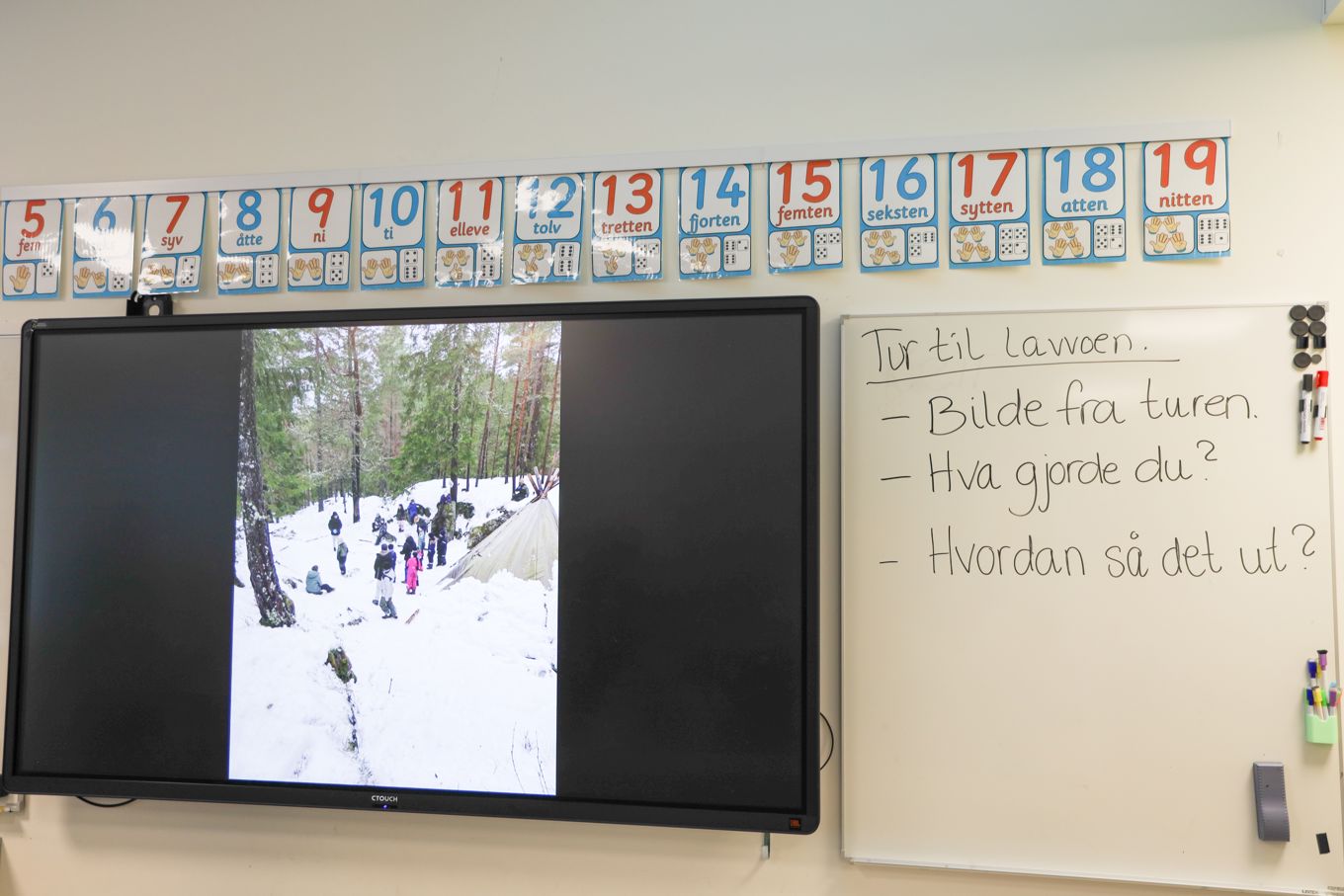 En digital tavle med bilde fra felles turopplevelse, og kriterier for oppgaven skrevet på whiteboard. 