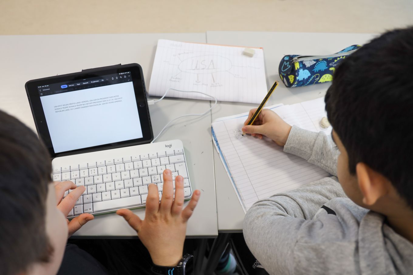 En elev skriver på tastatur, en annen elev skriver med blyant