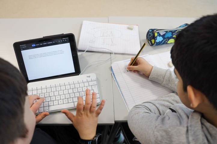 En elev skriver på tastatur, en annen elev skriver med blyant